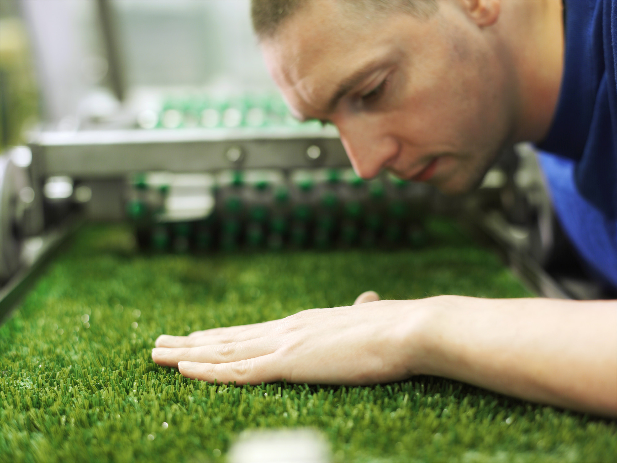 Worker inspecting artificial turf by running a hand over the grass fibers during testing..